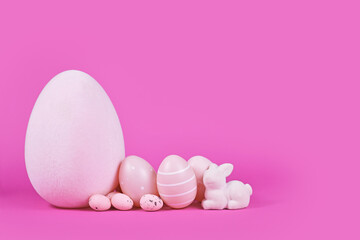 Easter eggs and small bunny sculpture on pink background with copy space
