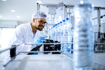 Technologist working in bottling factory doing quality control of drinking water before...