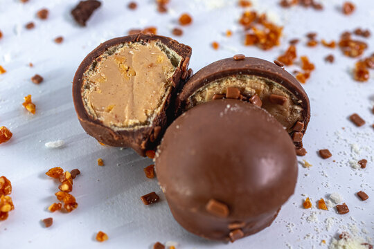 Bombom de chocolate com amendoim cortado ao meio sobre fundo branco com granulados doces ao redor