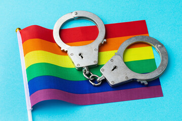 Handcuffs and a rainbow flag on a colored background, a concept on the topic of violation of the...