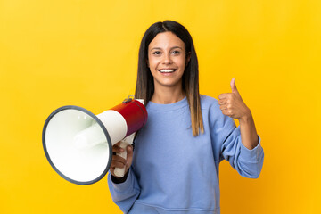 Caucasian girl isolated on yellow background holding a megaphone with thumb up