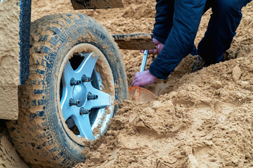 A man digs sand from under the wheel of a stuck car. Close-up.