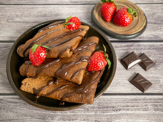 Pancakes made of chocolate dough with strawberries, poured with chocolate. Maslenitsa, a delicious sweet dessert.