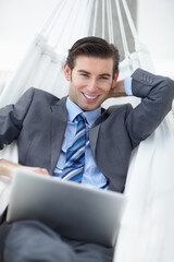 Relaxing business venture. A young businessman lying on a hammock while working on his laptop.