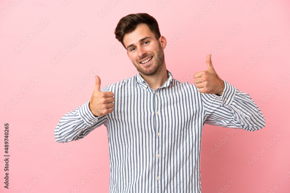 Wall mural Young caucasian handsome man isolated on pink background giving a thumbs up gesture