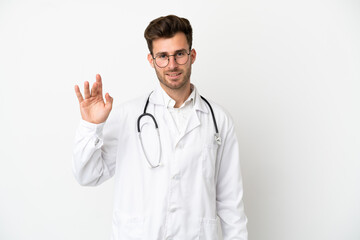 Fototapeta premium Young doctor caucasian man over isolated on white background wearing a doctor gown and saluting