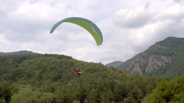 Paragliding. Extreme sport. Paraglider flying in the sky above beautiful green hills. 4k