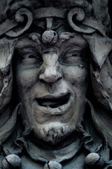 Evil clown and crazy joker. Fragment of an ancient stone statue. Close up.