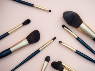 Assortment of female make-up of various face brushes. A set of professional dark blue and golden makeup brushes on a pink background.