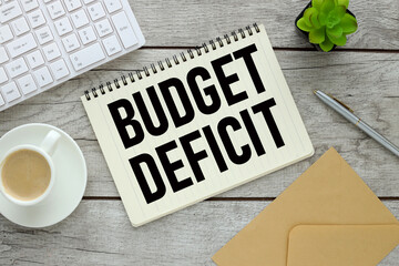 BUDGET DEFICIT. notepad with text on a wooden table and a cup of coffee. plant keyboard envelope. working table