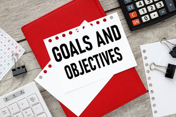 GOALS AND OBJECTIVES text on notepad with pen on wooden background