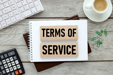 TERMS OF SERVICE, text on a notepad on wooden blocks with a calculator and a cup of coffee. wooden background