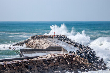 big ocean wave hit in a jetty from a pier in a stormy day
