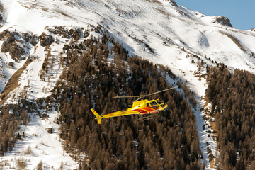 A yellow helicopter fying in the swiss alps