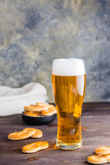 Glass of beer with foam and salty pretzels on a wooden table. Vertical view