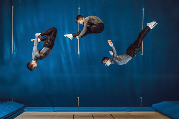 Youn man doing different pirouettes in elastic bed in mid-air. Blue background, collage © Guindilla y Pimienta
