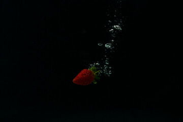 Strawberry falling into water with splash on black background