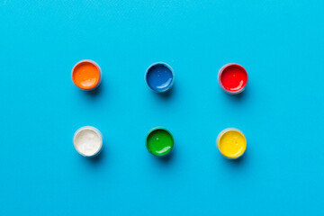 jars with gouache of different colors on Colored background. hobby painting. Top view with empty space. workplace for creativity. home teaching concept drawing