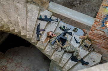 Caucasian woman in military uniform lies on the stairs of an abandoned building and holds a machine gun. View from above. 