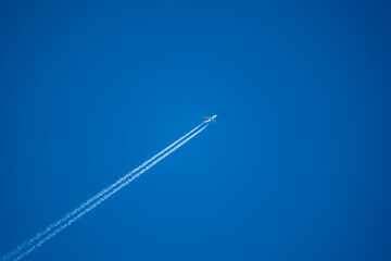 looking up at a twin engine jet airliner in deep blue sky leaving long contrails as it moves diagnolly across the frame