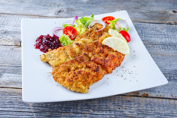 Traditional deep-fried schnitzel with green salad, tomatoes and cranberry jam served as close-up on...