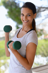 Fresh air and a great workout. Portrait of a beautiful woman lifting dumbbells by a window.