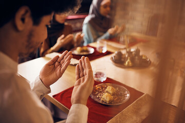 Close-up of Muslim man praying with his family at dining table.