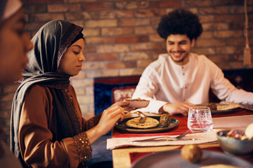 Young Middle Eastern woman eats with her family at dining table at home.