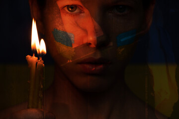 Stop the war in Ukraine. A girl with a candle in her hands prays against the background of a ground...