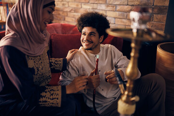 Fototapeta na wymiar Happy Muslim man drinks Turkish tea with his wife while smoking hookah.