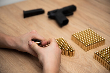 Mężczyzna wkładający naboje do magazynka, w tle leży broń i naboje na stole