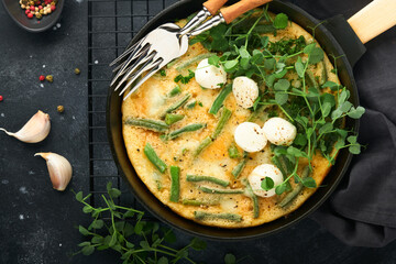 Frittata. Omelet with spinach and green beans, healthy food in black frying pan on dark old rustic background. Healthy breakfast delicious. Top view flat lay. Copy space.