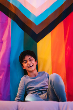 Ethnic boy sitting on bed near rainbow flag