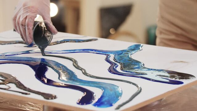 Pours grey epoxy resin on canvas from a plastic container