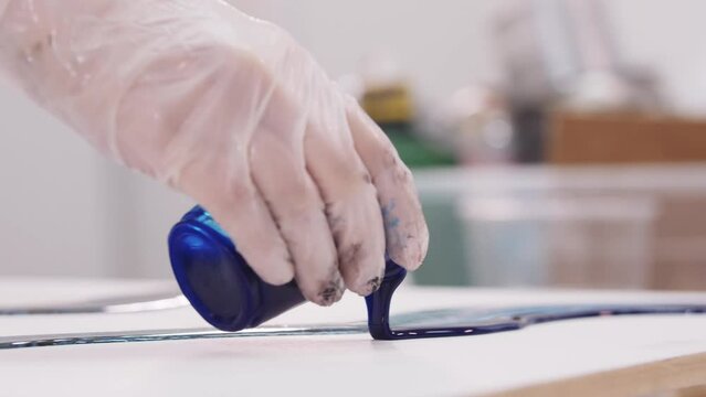 Artist pours deep blue epoxy resin on canvas