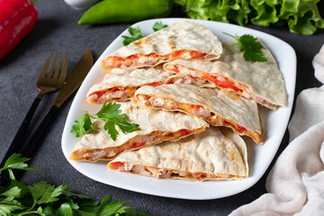 Mexican snack quesadilla from tortilla with bacon, chicken, cheese and pepper in white plate on gray background