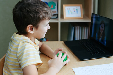 8 years old boy sit by desk with laptop and do exercise with massage ball