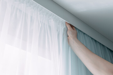 Close up of hands hanging curtain on ceiling ledge. Interior decor element. Curtain interior decoration in living room.