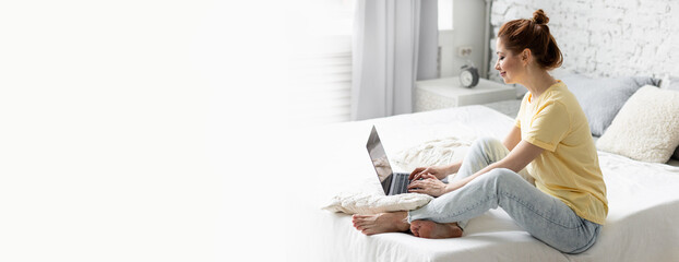 Beautiful young woman working remotely or studying at home at her laptop in her bedroom. Banner, copy space for text