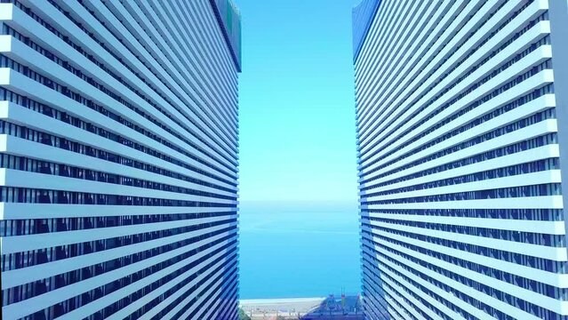 the drone passes through two buildings of a skyscraper on the background of the sea or ocean. it flies through hotels with panoramic mirrored windows. Real estate business. Finance and architecture.
