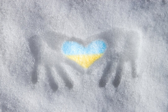 on the snow are handprints that have formed into a sign of the heart. the heart is painted in the colors of the Ukrainian flag: yellow and blue. concept no war.