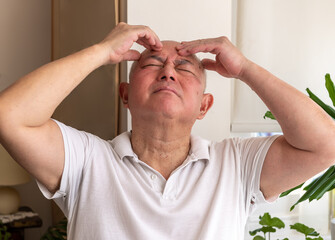 A matured senior man at home pinching and rubbing his head feeling unwell and or in pain. Feeling...