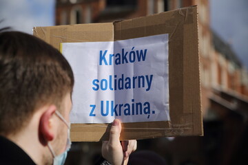 man holding a cardboard box text KRAKOW SOLIDARITY WITH UKRAINE in Polish during public protest
