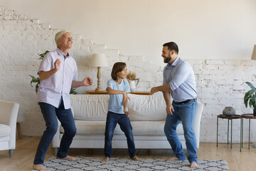 Little boy his older active grandfather, young father dancing barefoot in warm living room, listen...