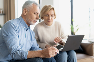 Middle-aged spouses with laptop and credit card