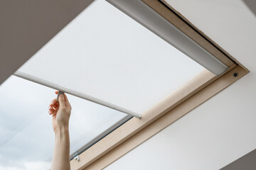 Woman hand open blinds on attic or mansard window