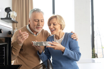 Smiling senior couple taking dish out of oven