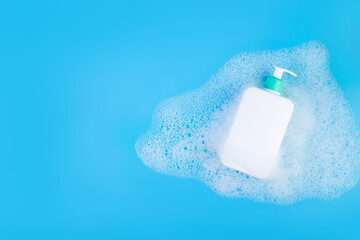 Flatlay view closeup organic gentle facial skincare, сleansing micellar foaming water product cleanser white tube with a blank label on blue background on bath foam bubbles texture as a background