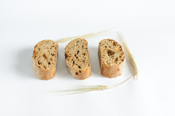 Three pieces of dark bread on a white plate with ears of rye. Selective focus with copy space, natural light. View from a high angle