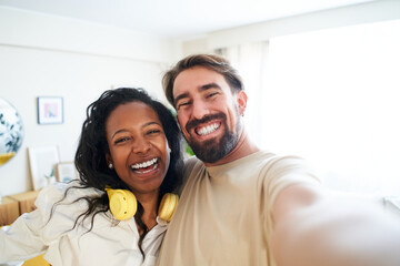Cheerful selfie at home mixed race couple smiling and looking at camera. Happy man and beautiful...
